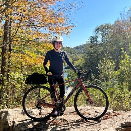 Janelle K. standing with her bicycle on a trail in autumn.
