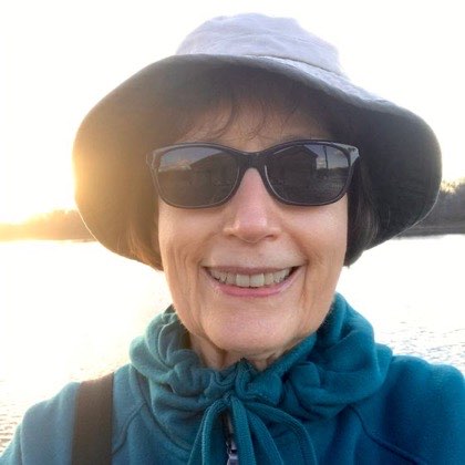 Judy S., 75, outdoors in a sun hat by the water.