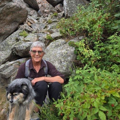 Virginia C., 69, crouched on a rocky wilderness trail beside her dog.
